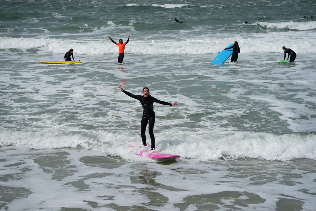 Een meisje surft op een roze surfboard met haar handen omhoog.