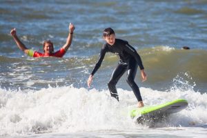Surfinstructor juicht en surfer surft op groen surfboard met de golf